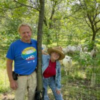 Tom and Kathy standing in front of a pen of sheep in a forest