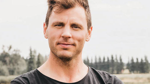 Man in a grey tshirt standing in front of an orchard
